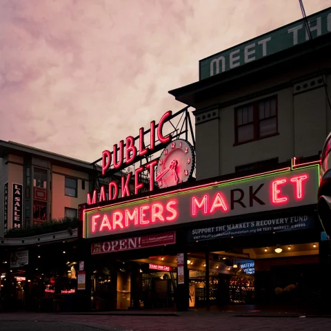 neon sign reads, "public market" and "farmers market" under purple sunset