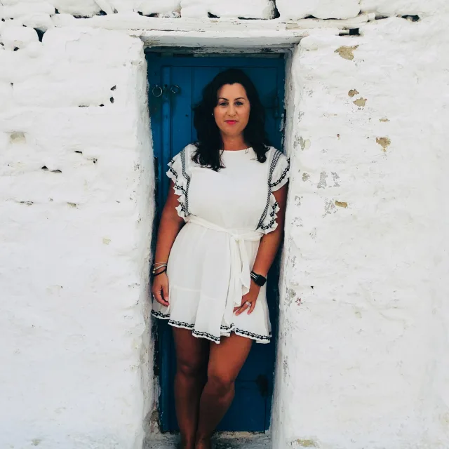 Travel Advisor Kristy Rudolph in a white dress in front of a white wall and blue door.