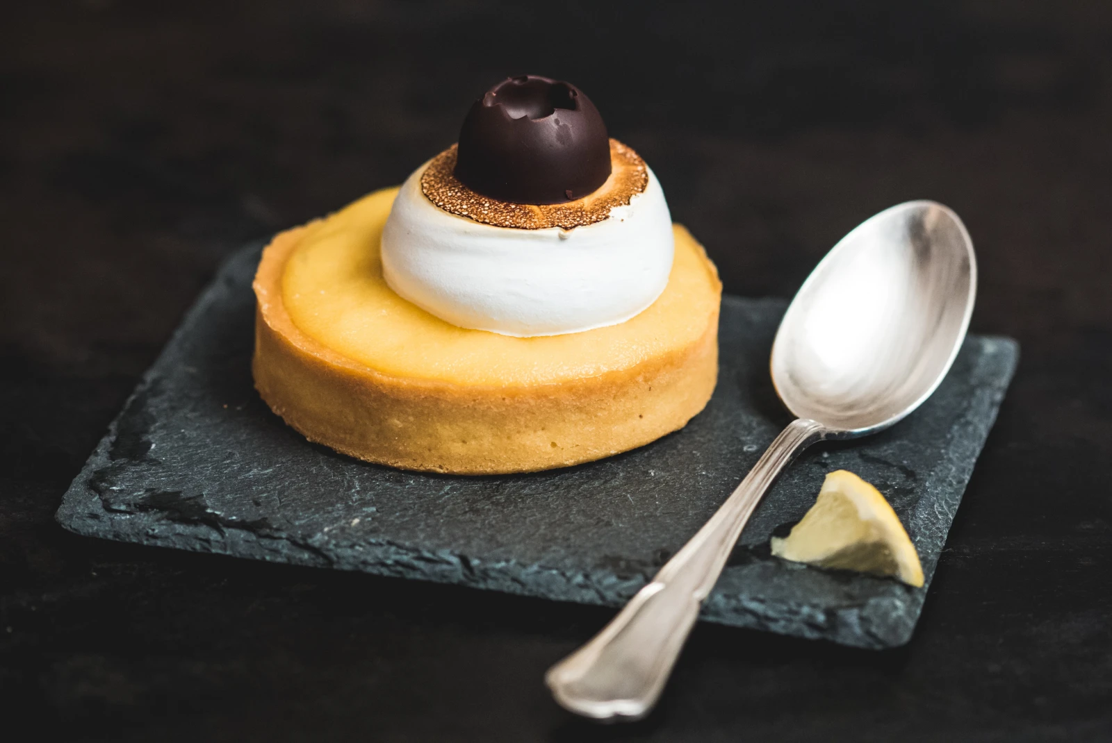 Pastry with yellow custard with white and black topping on a black slate plate with a silver spoon