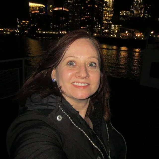 Picture of Nicole on a ferry wearing a black winter coat in front of the Boston skyline at night 