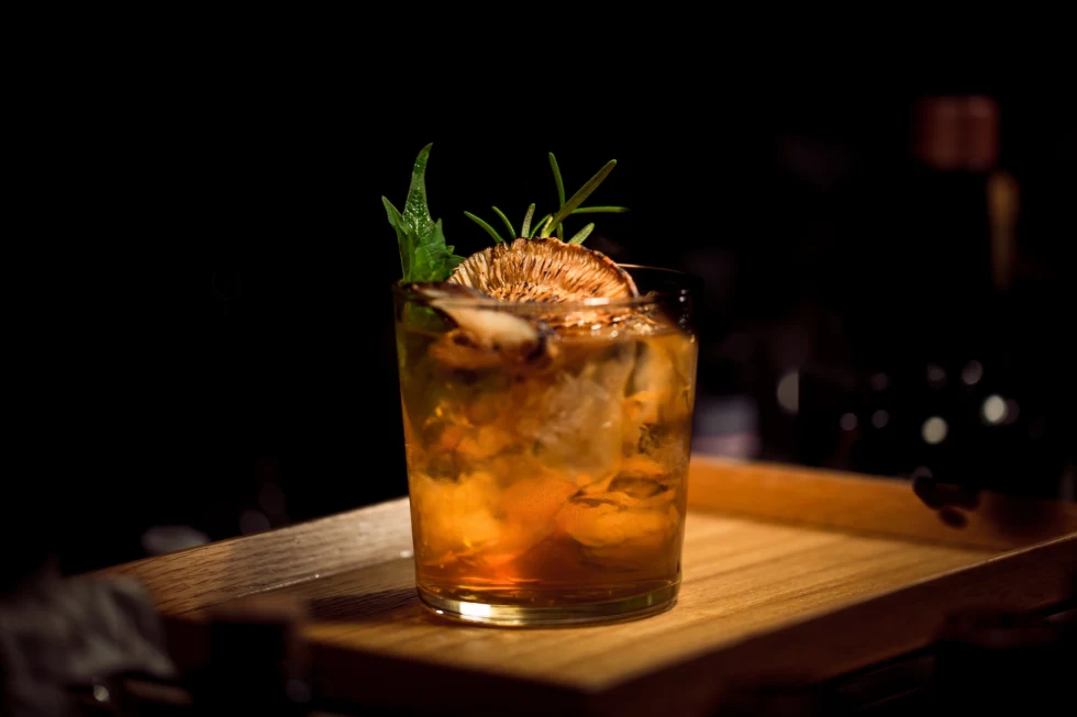 up-close shot of a whiskey cocktail garnished with a dried orange slice and herbs