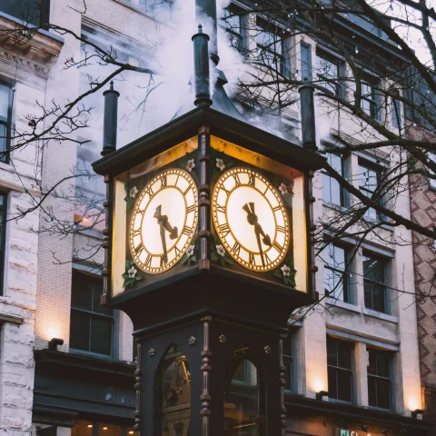 A picture of a brown wooden analog clock on the streets.