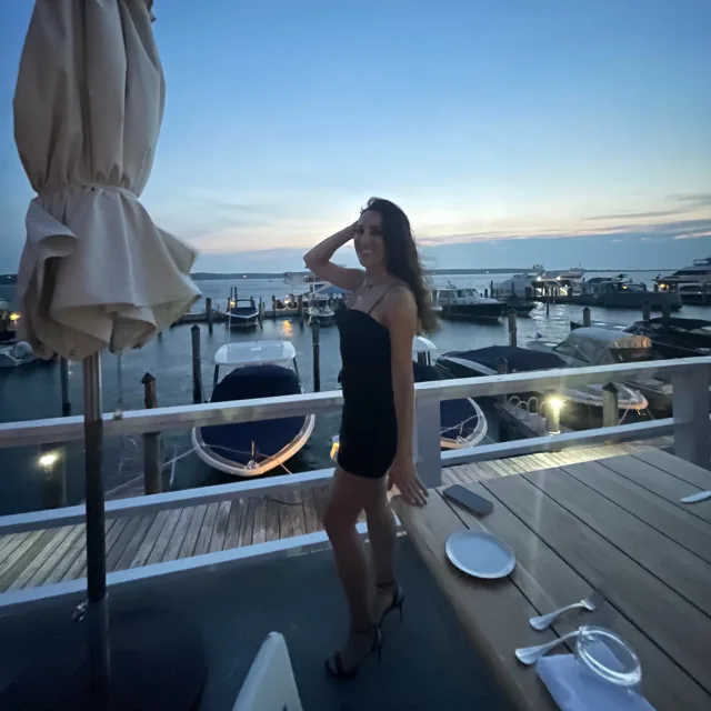 Michelle posing in a black dress near an umbrella and a harbor at dusk