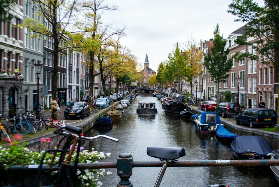 canal through an old city lined with boats and trees on the shore