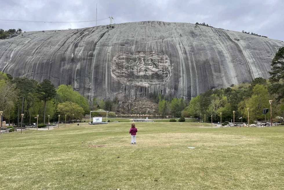 Grey Stone Mountain in Atlanta, Georgia with a child in red standing on green grass.