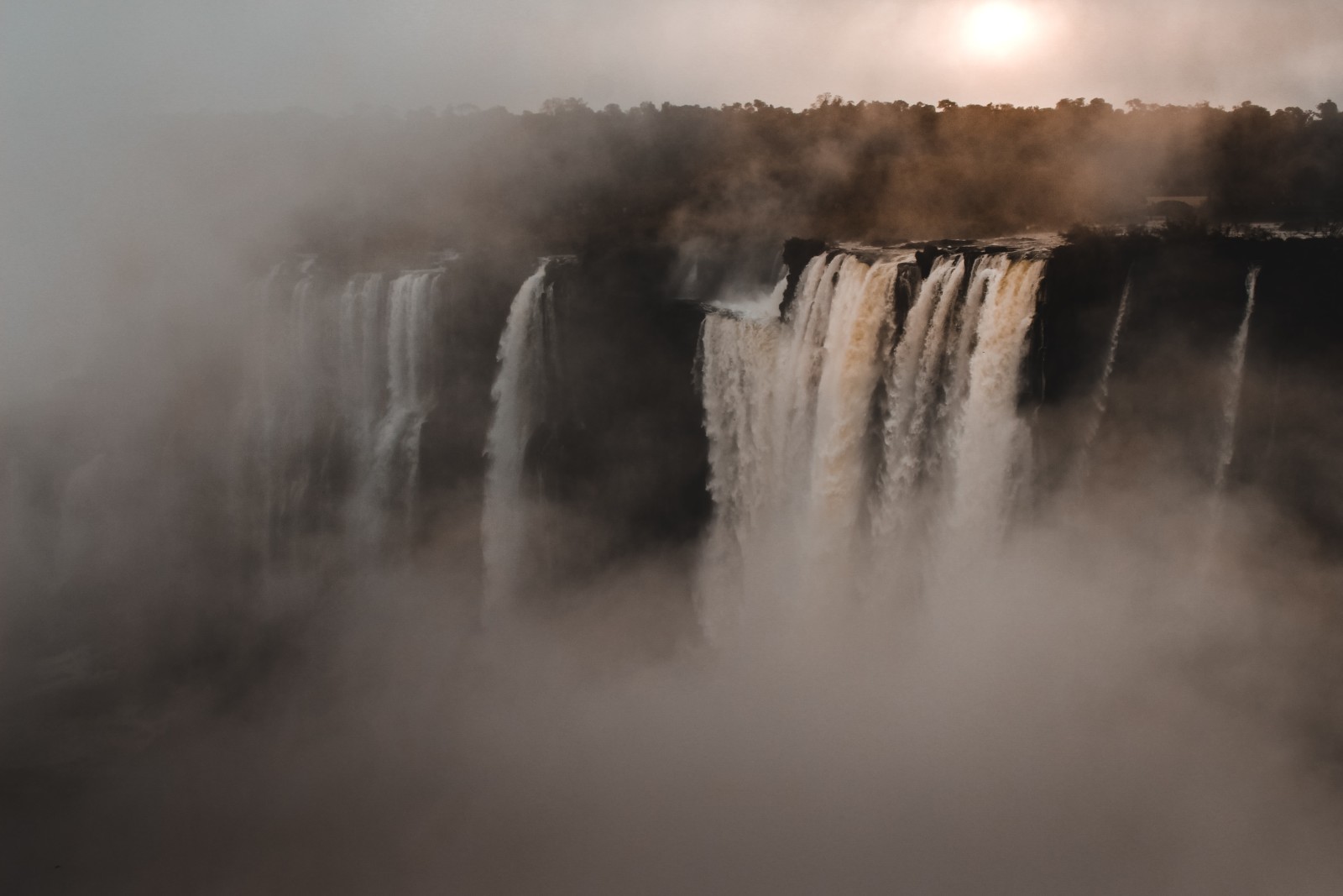 Misty waterfalls with white gushing water and a bright sun at Devil’s Throat on the Argentina side.