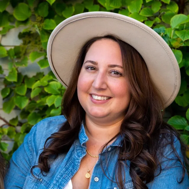 Travel Advisor Deanna Cirola with a tan hat, jean jacket and green leaves.