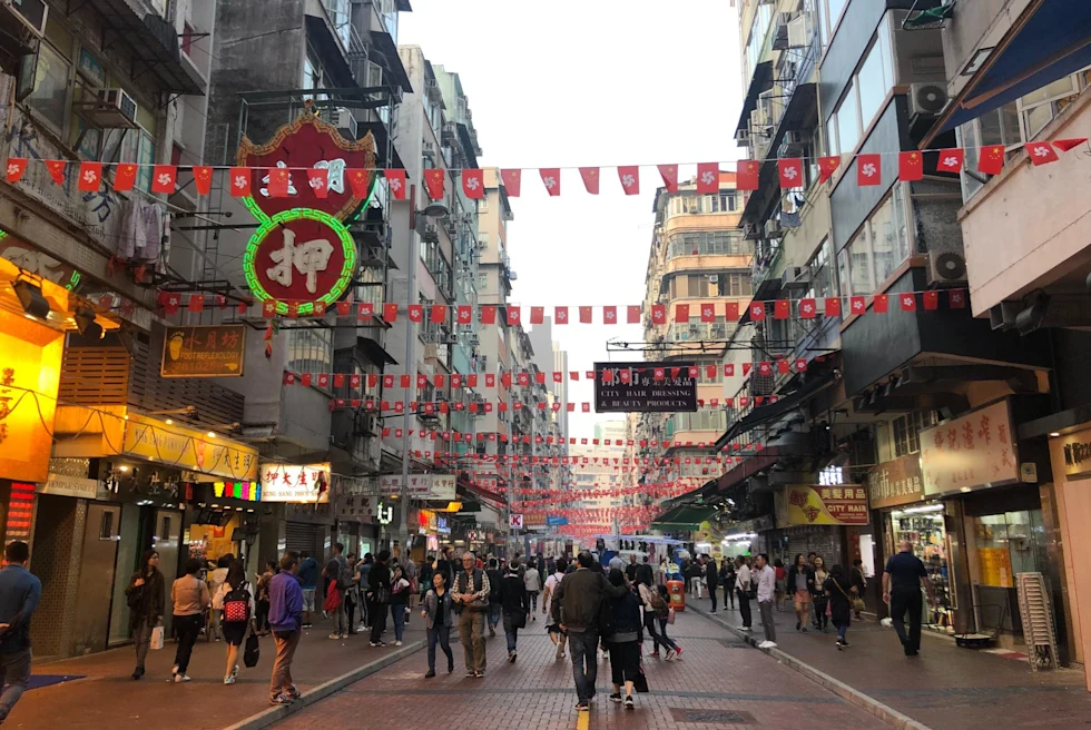 busy city street market with red flags strung across the buildings on a gray day