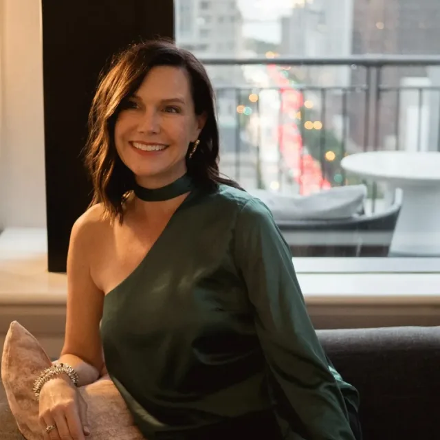 Travel Advisor Sandra Perry with a green one-shoulder dress and black choker in front of a window.