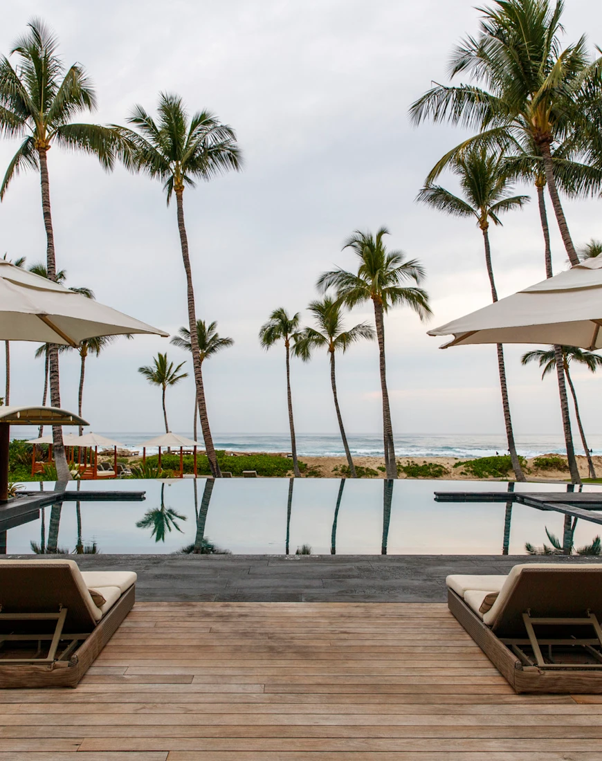 two lounge chairs on a wooden deck overlooking an oceanfront pool