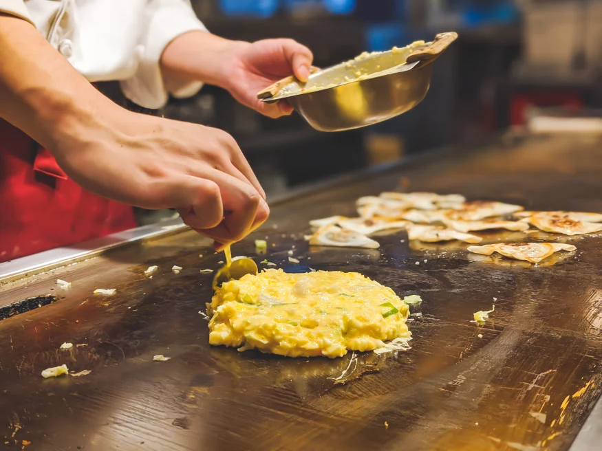 Person preparing okonomiyaki on flat top in Osaka