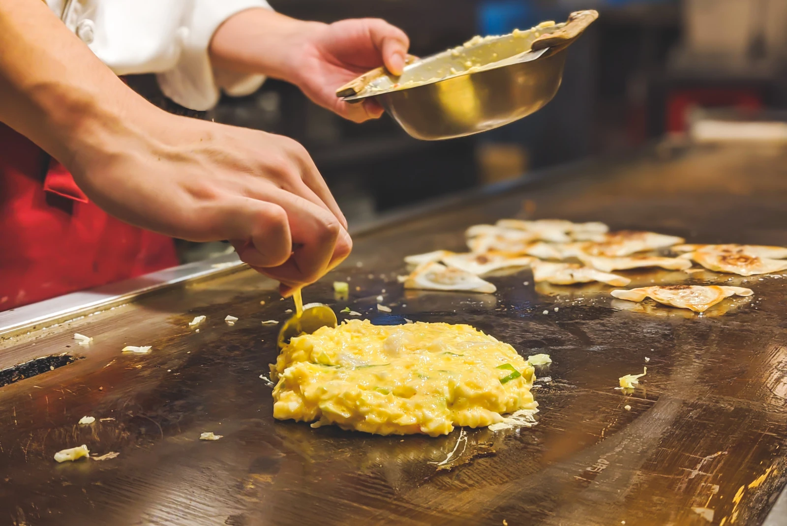 Person preparing okonomiyaki on flat top in Osaka