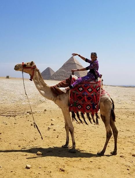 Woman sitting on camel with pyramid in the background