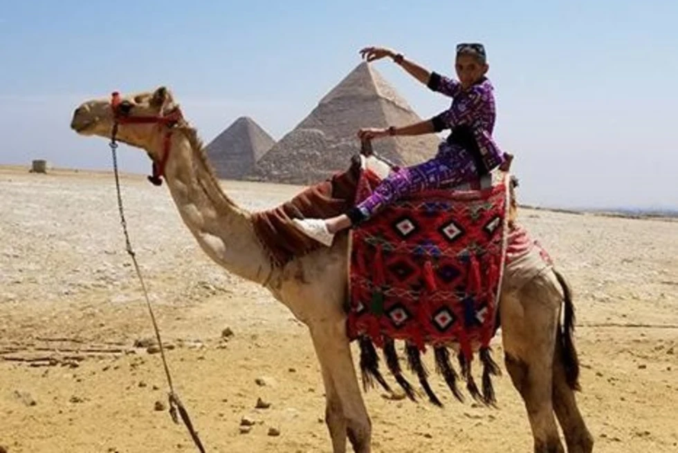 Woman sitting on camel with pyramid in the background
