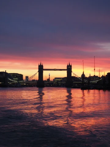 Tower of London bridge during a purple yellow and oranage sunset reflecting on the canal