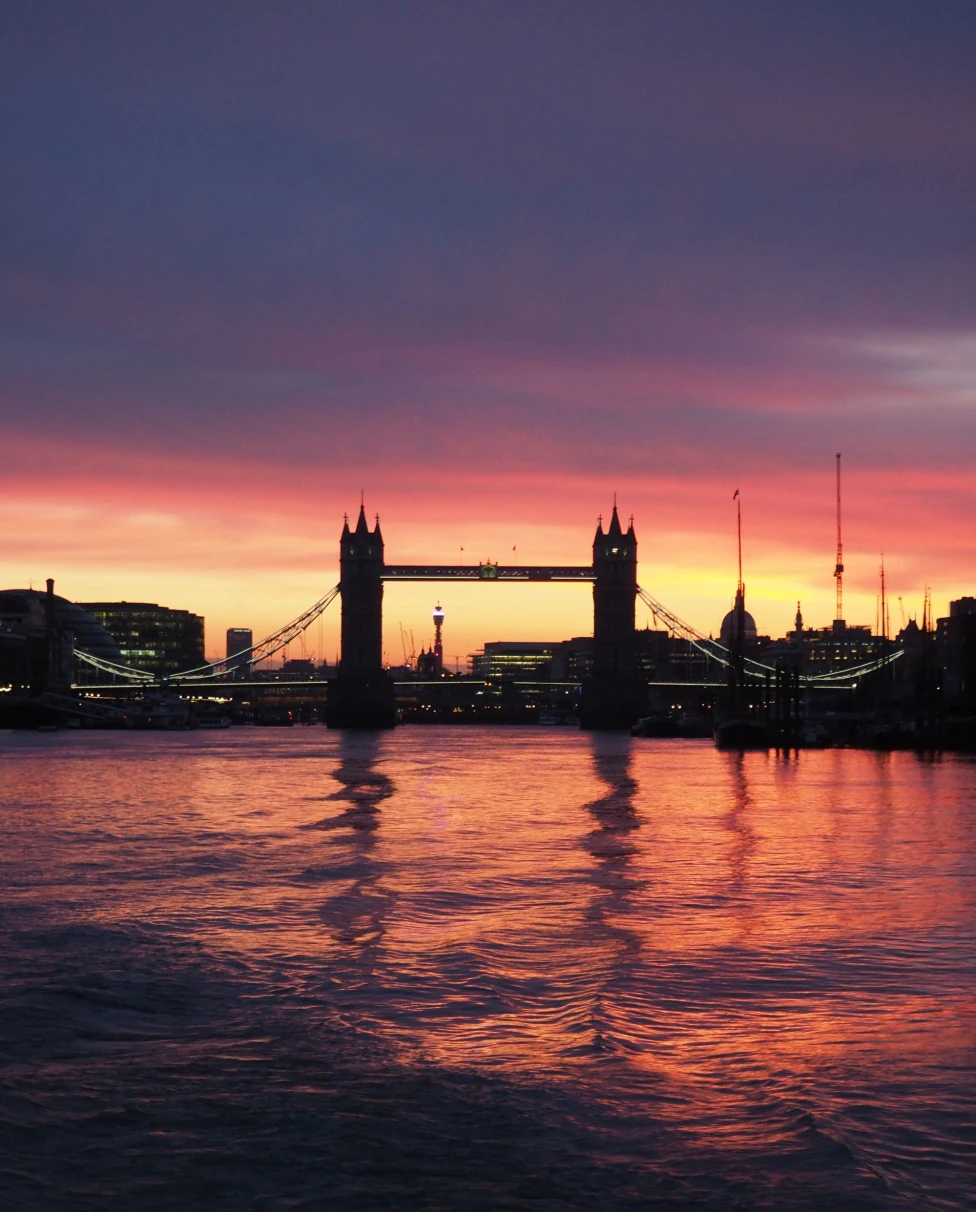 Tower of London bridge during a purple yellow and oranage sunset reflecting on the canal