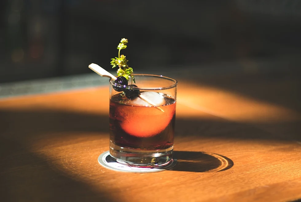 small glass with brown liquor and garnished with herbs