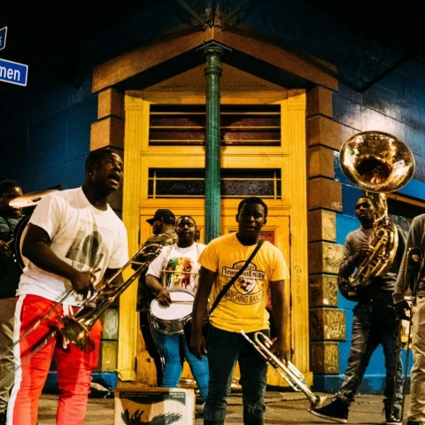 A group of people playing instruments outside in front of a yellow and blue building at nighttime. 
