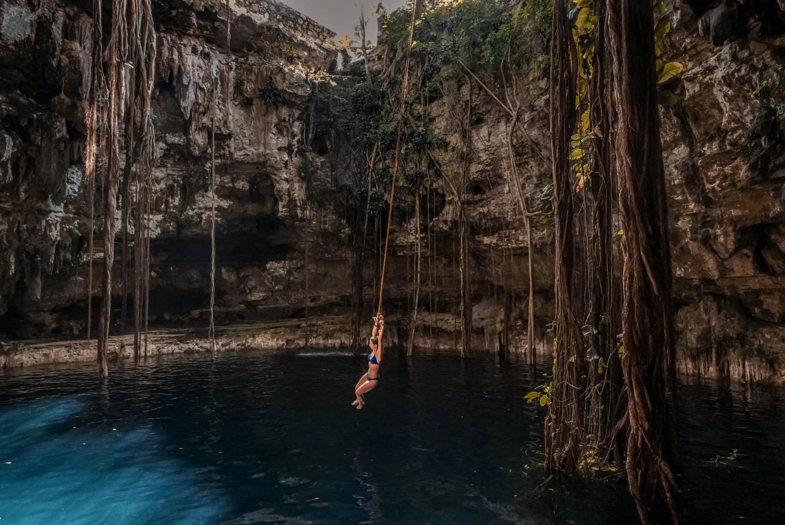 Girl swinging from rope to jump into a Cenote in Tulum.