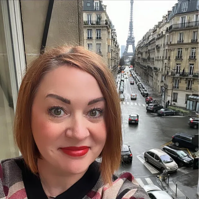 Travel Advisor Michelle Darcy stands on a balcony in Paris with a view of the Eiffel Tower in the distance. 