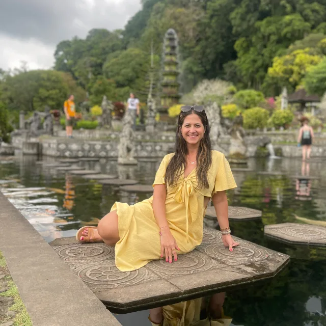 Picture of Mariela in a yellow dress in front of a temple and water surrounded by trees