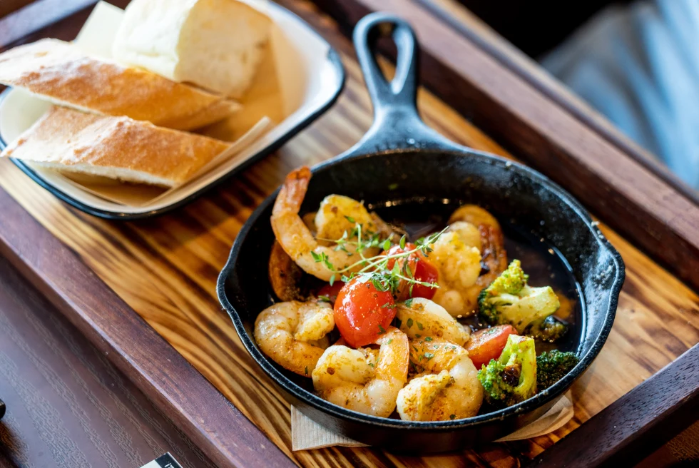 shrimp with tomato and broccoli in a small black cast iron skillet with three pieces of cut baguette on a wooden tray