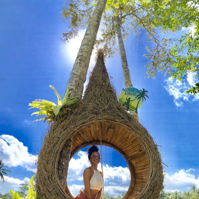 Fora travel agent Courtney Aki sitting in a brown treehouse with blue skies and green palm trees.