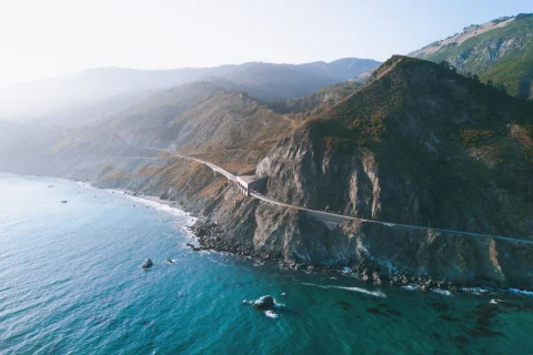 The scenic coast of Big Sur, with the Pacific Coast Highway running along the cliffs beneath fog-covered hills (photo by Thomas Ciscewski)