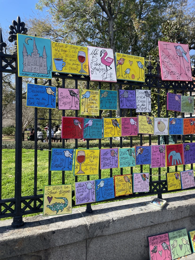 A view of colorful cards hanging on a metal fence outside. 