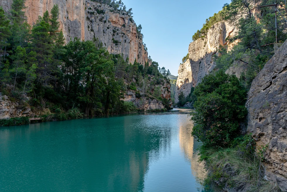 blue water in Montanejos Spain with red and brown rocks and green trees