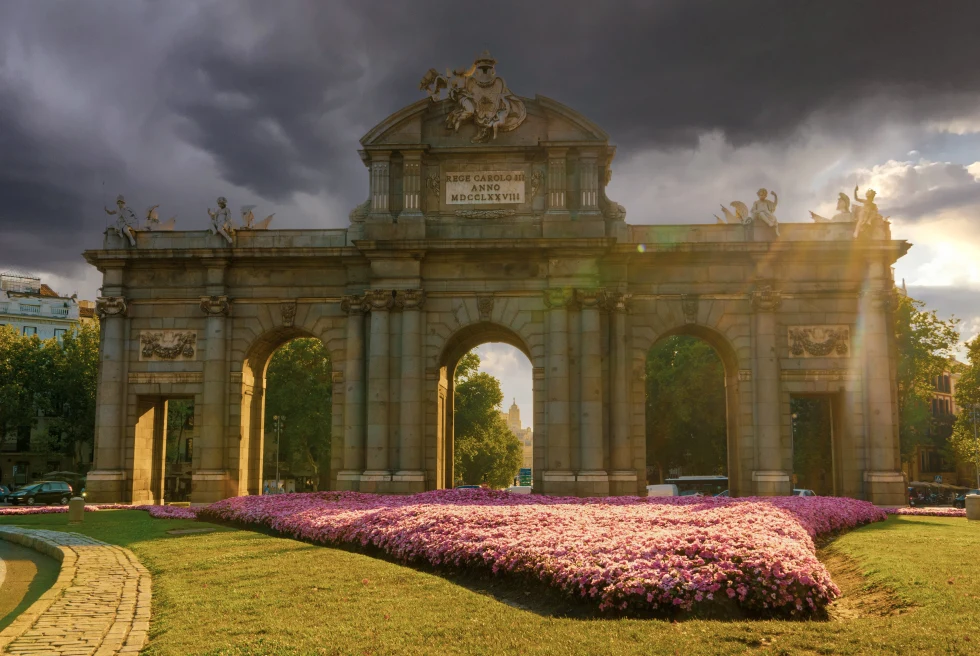 Large stone statue next to green space and purple flowers during daytime