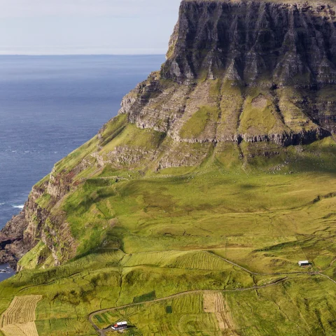 an island of green fields with a small village and grass covered cliffs over the ocean