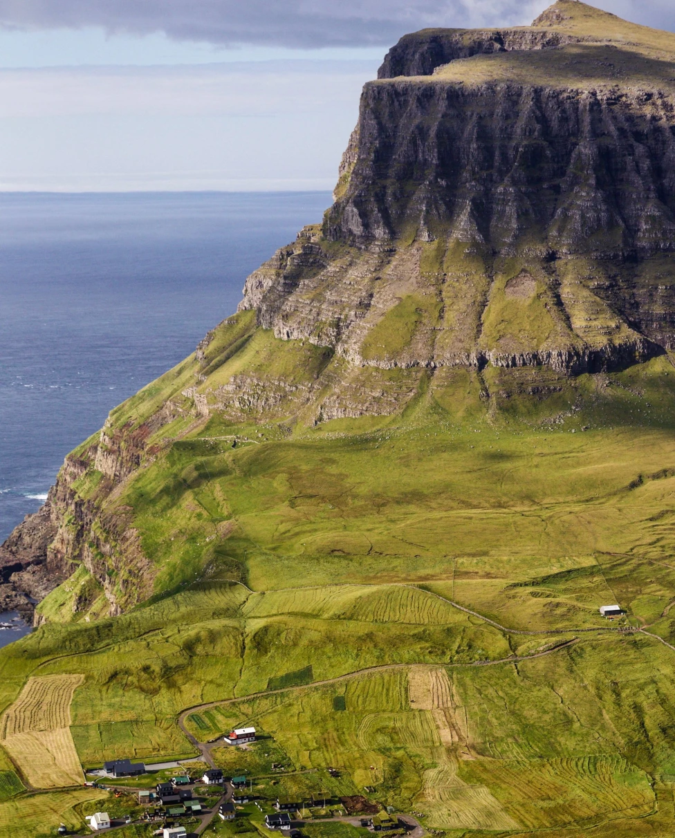 an island of green fields with a small village and grass covered cliffs over the ocean