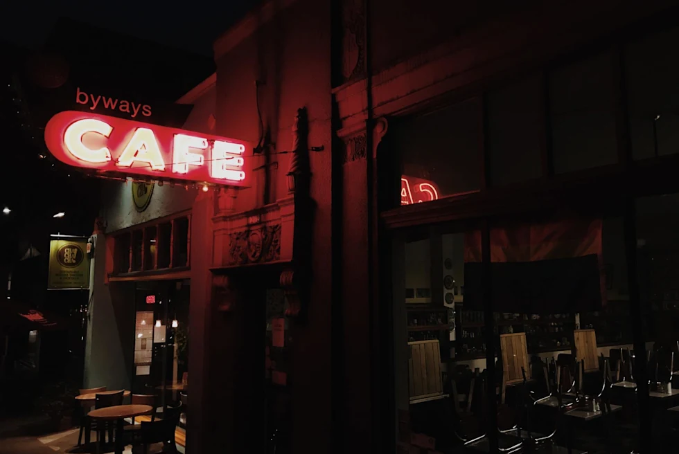 red neon sign reads, "cafe" outside a dark bar