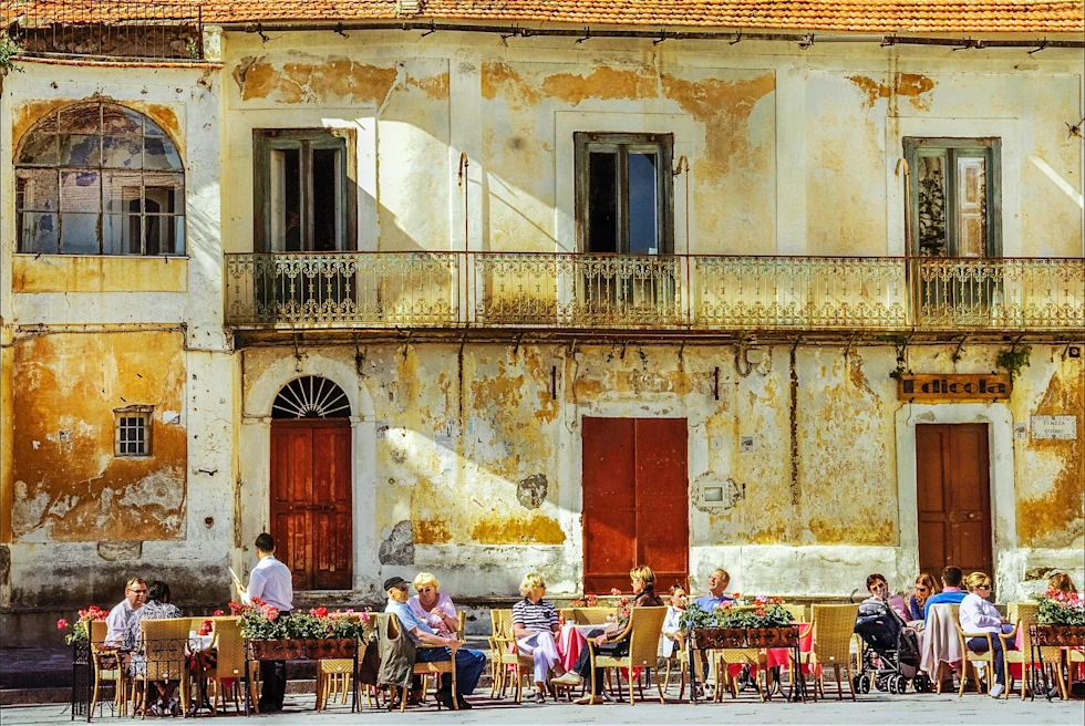 A street with coffee table and people against an old building in Ravello.