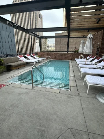 The rooftop pool at Virgin Hotels New Orleans with white sun loungers and umbrellas and a concrete floor and dark beams overhead