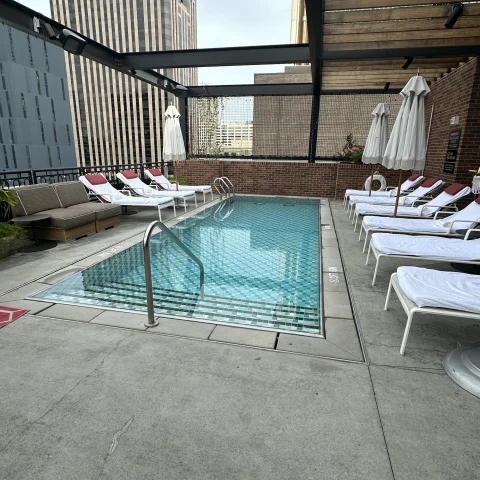 The rooftop pool at Virgin Hotels New Orleans with white sun loungers and umbrellas and a concrete floor and dark beams overhead