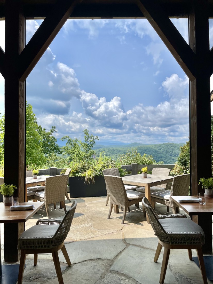 A restaurant patio with dining chairs, a wooden archway and a view of the mountain range in the distance. 