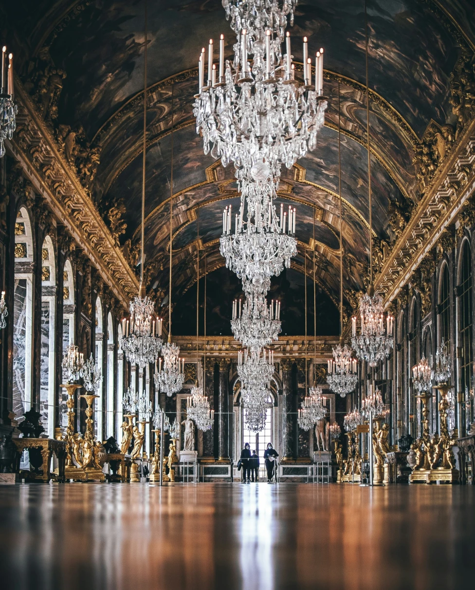 A picture of people walking in a building with huge chandelier.