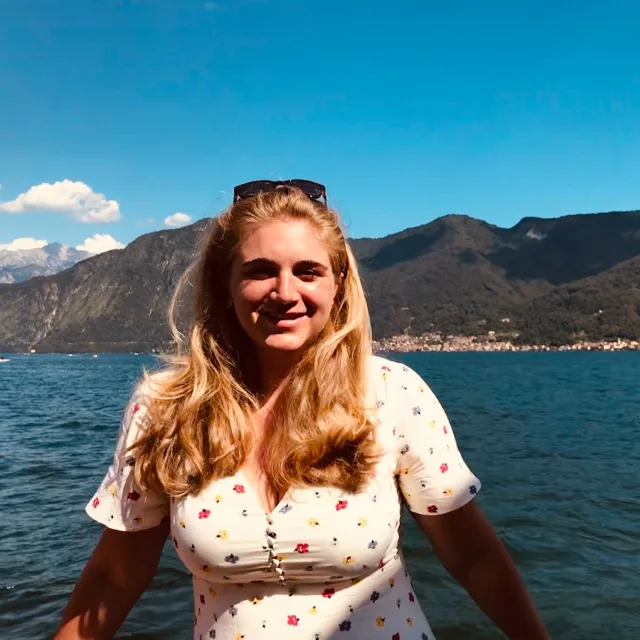 Travel Advisor Laura Bleeke with pink floral dress in front of blue water and green mountains.
