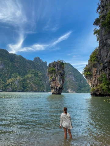 Isabel standing in water with her back to the camera facing a rock formation on James Bond Island.