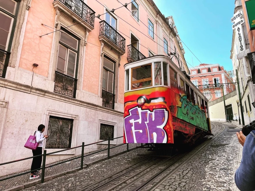 a funicular painted with graffiti travels up a steep stone hill on a city street