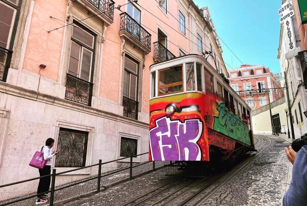 a funicular painted with graffiti travels up a steep stone hill on a city street