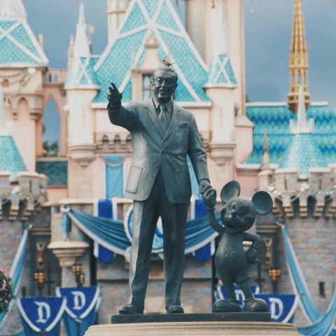 A statue of Walt Disney with an outstretched arm next to Mickey Mouse in front of Cinderella's castle, close to some of the best hotels to stay near Disneyland.
