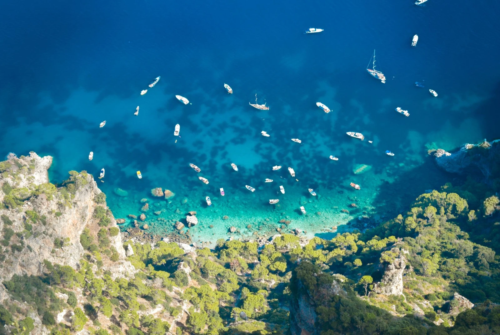 aerial view of an island coast with bright blue waters spotted by white boats