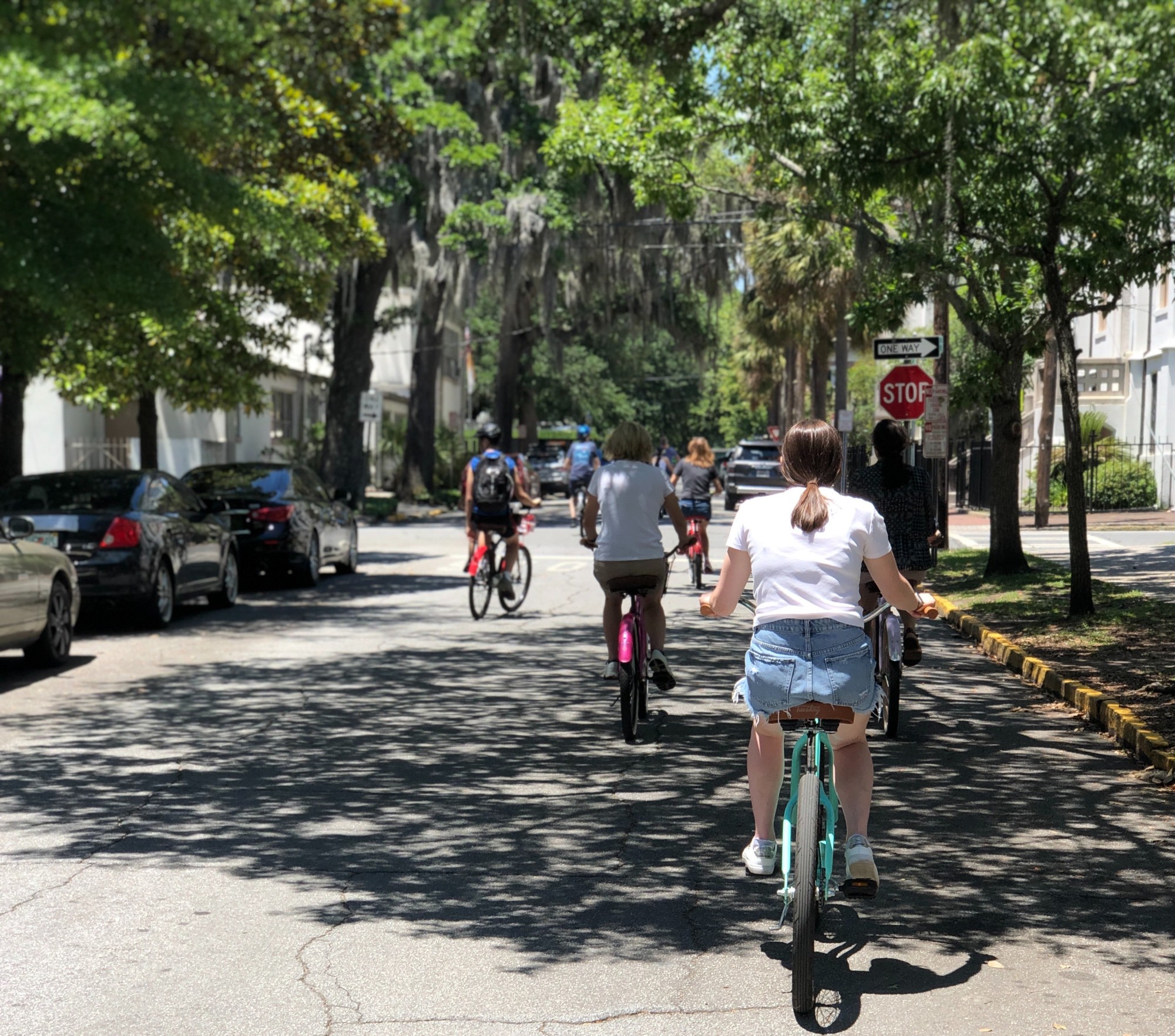 people bike down a quiet suburban street with sun making shadows through the trees