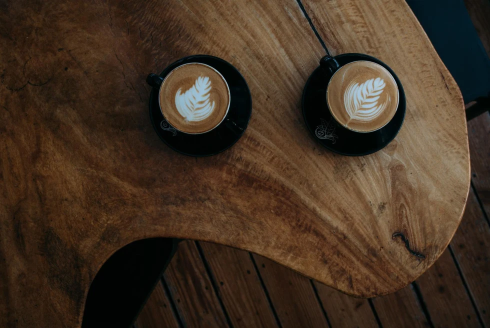 two lattes with milk art in black mugs sit on wooden table