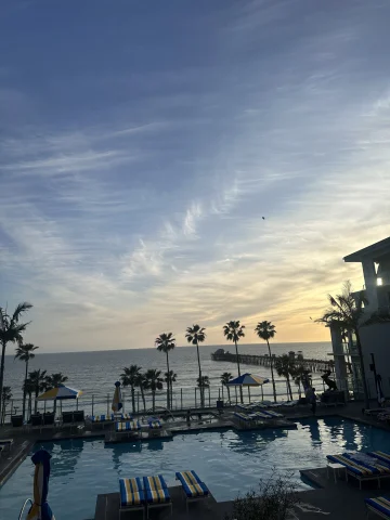 A view of a hotel pool next to the ocean during a sunset