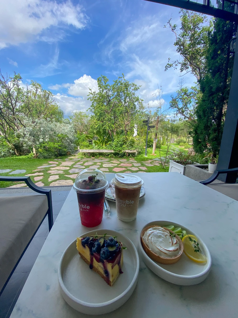 A patio table with two plates of breakfast pastries and two to-go coffee drinks overlooking a garden at Double You Cafe.