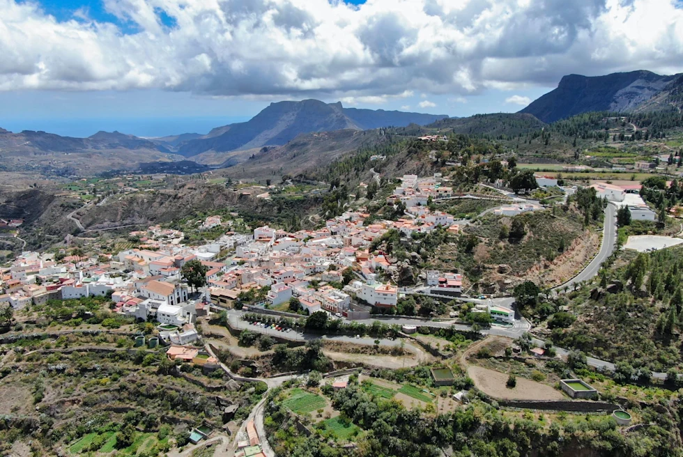 a town nestled within mountain range with surrounding vineyards and fluffy clouds in the sky
